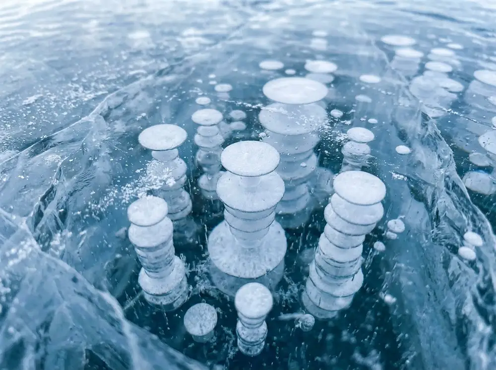 Gros plan sur des colonnes de bulles de méthane blanches figées en couches successives dans la glace transparente du lac Abraham