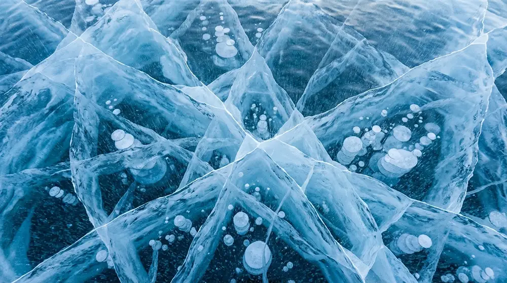 Fissures profondes et géométriques dans la glace épaisse du lac Abraham avec des bulles de méthane visibles en profondeur