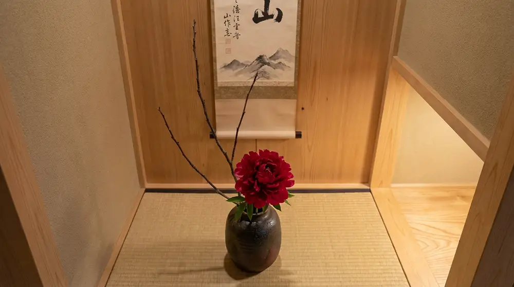 Arrangement ikebana minimaliste avec une pivoine rouge dans un vase en céramique posé dans une alcôve tokonoma japonaise
