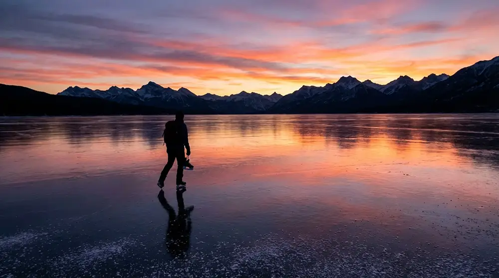Patineur solitaire en silhouette sur la glace du lac Abraham au coucher du soleil avec les montagnes en arrière-plan