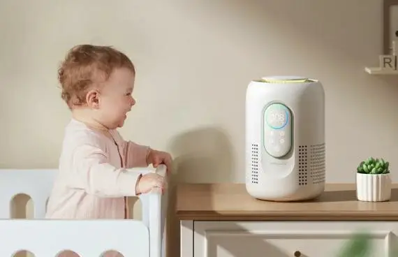 bébé souriant debout dans son lit et regardant le purificateur d'air posé sur la table d'à côté