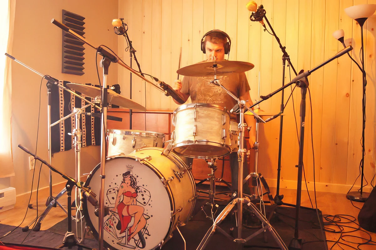 Batteur qui enregistre en studio, entouré de micros