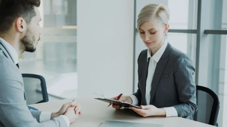 Employeur tenant un CV annoté sur la table et candidat assis en face pendant un entretien d'embauche
