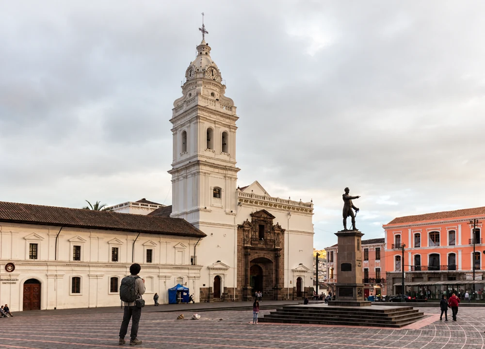 Voyager léger : mes conseils pour tout faire tenir dans un bagage cabine Voyageur de dos avec un petit sac à dos sur une place de Quito, en Équateur